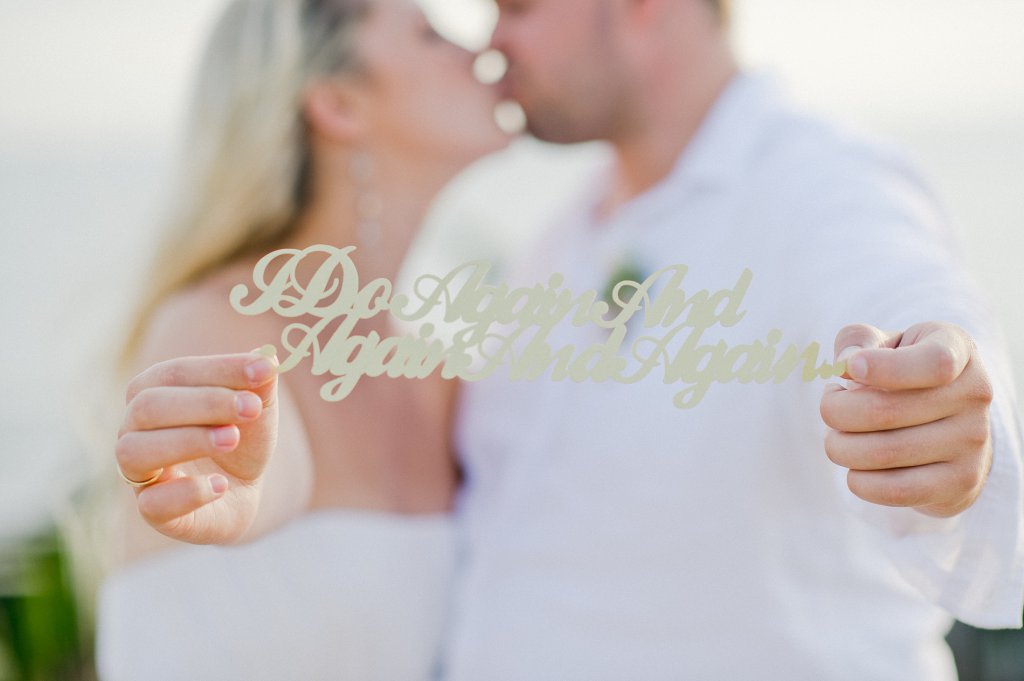 Photo Bride and groom kissing, holding up a singn reading 